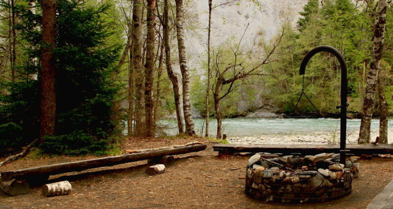 Grillstelle am Rhein mit Holzbänkli rundherum und Wald.