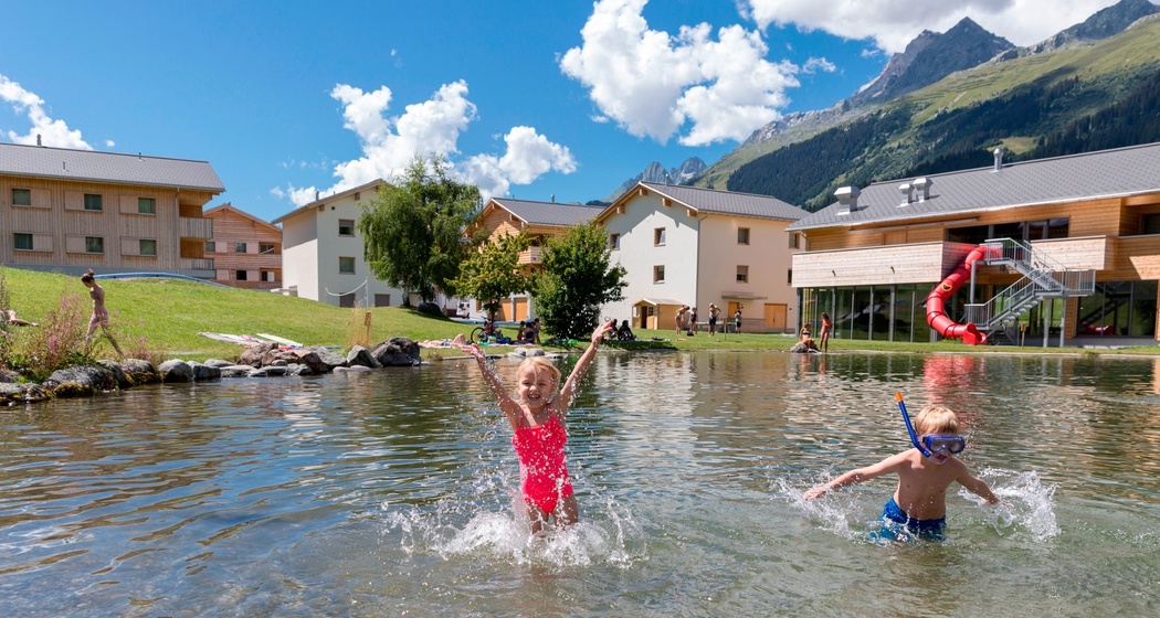 Das Foto zeigt den Badesee in Brigels und zwei kleine Kinde spielen im Wasser.