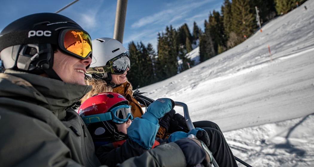 Das Foto zeigt eine Familie die auf dem Sessellift hinaufsteigen