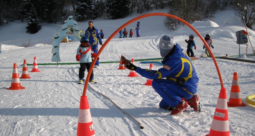 Das Foto zeigt einen Skilehrer der ein junges Mädchen das Skifahren beibringt