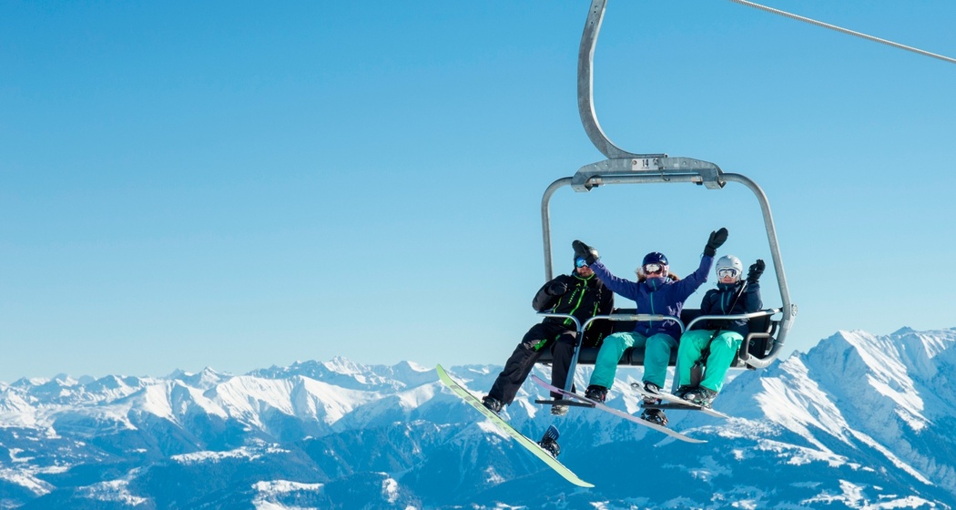 Das Foto zeigt drei Menschen die auf der vierer Sesselbahn hinaufsteigen