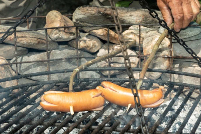Das Foto zeigt eine Feuerstelle und zwei Cervelats die am braten sind