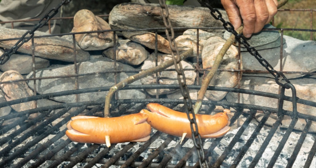 Das Foto zeigt eine Feuerstelle und zwei Cervelats die am braten sind
