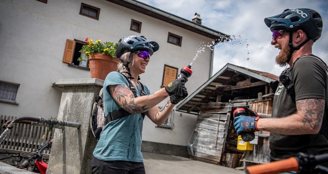 zwei Mountainbiker die eine Pause bei einem Brunnen machen