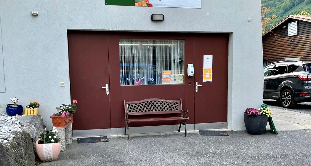 Eingang zum Hofladen Aeulehof mit rotem Tor, Sitzbank und Blumendekoration in Triesen, Liechtenstein.