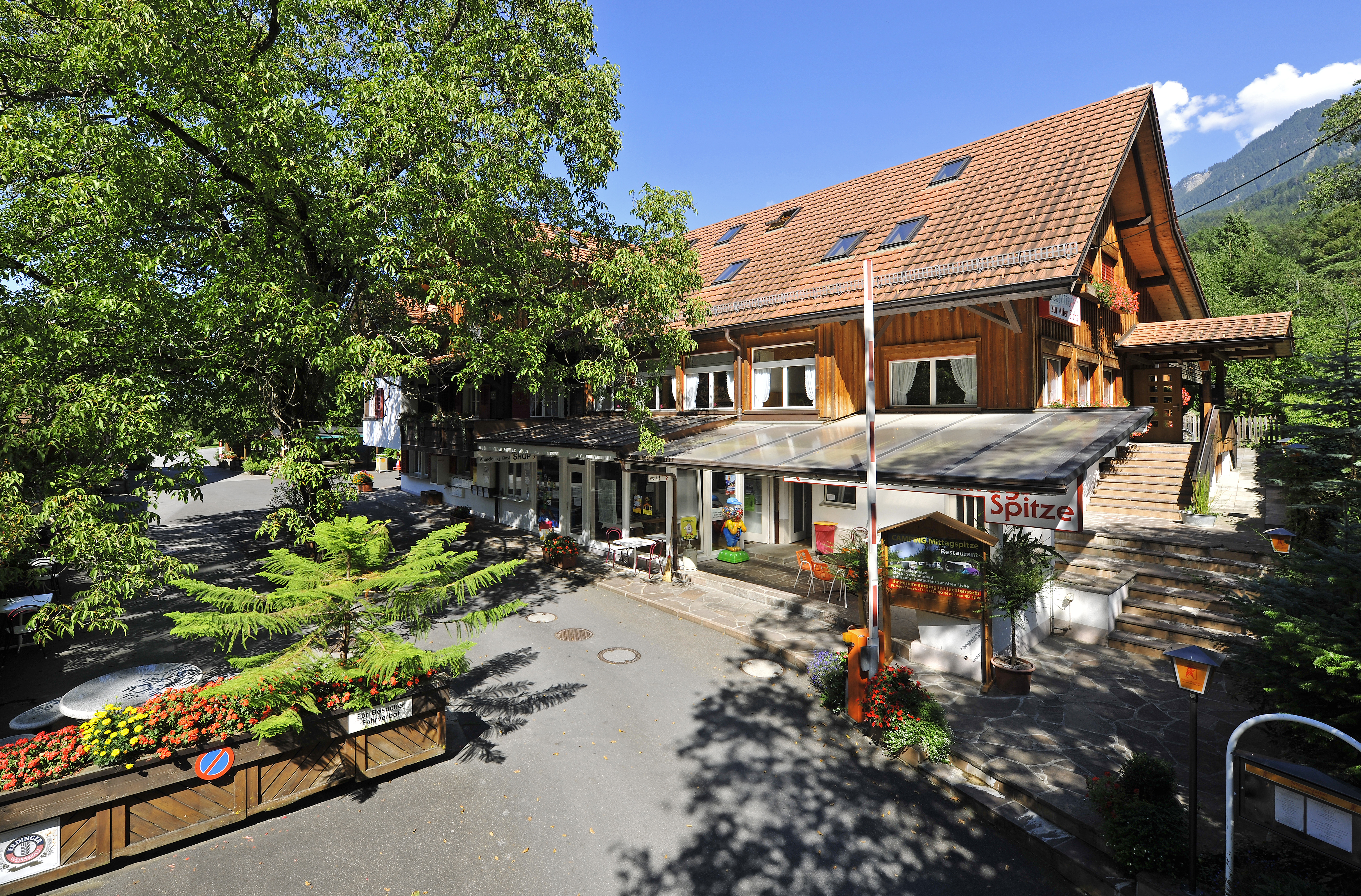 Außenansicht des Haupthauses des Campingplatzes Mittagsspitze mit Restaurant und schattiger Terrasse.