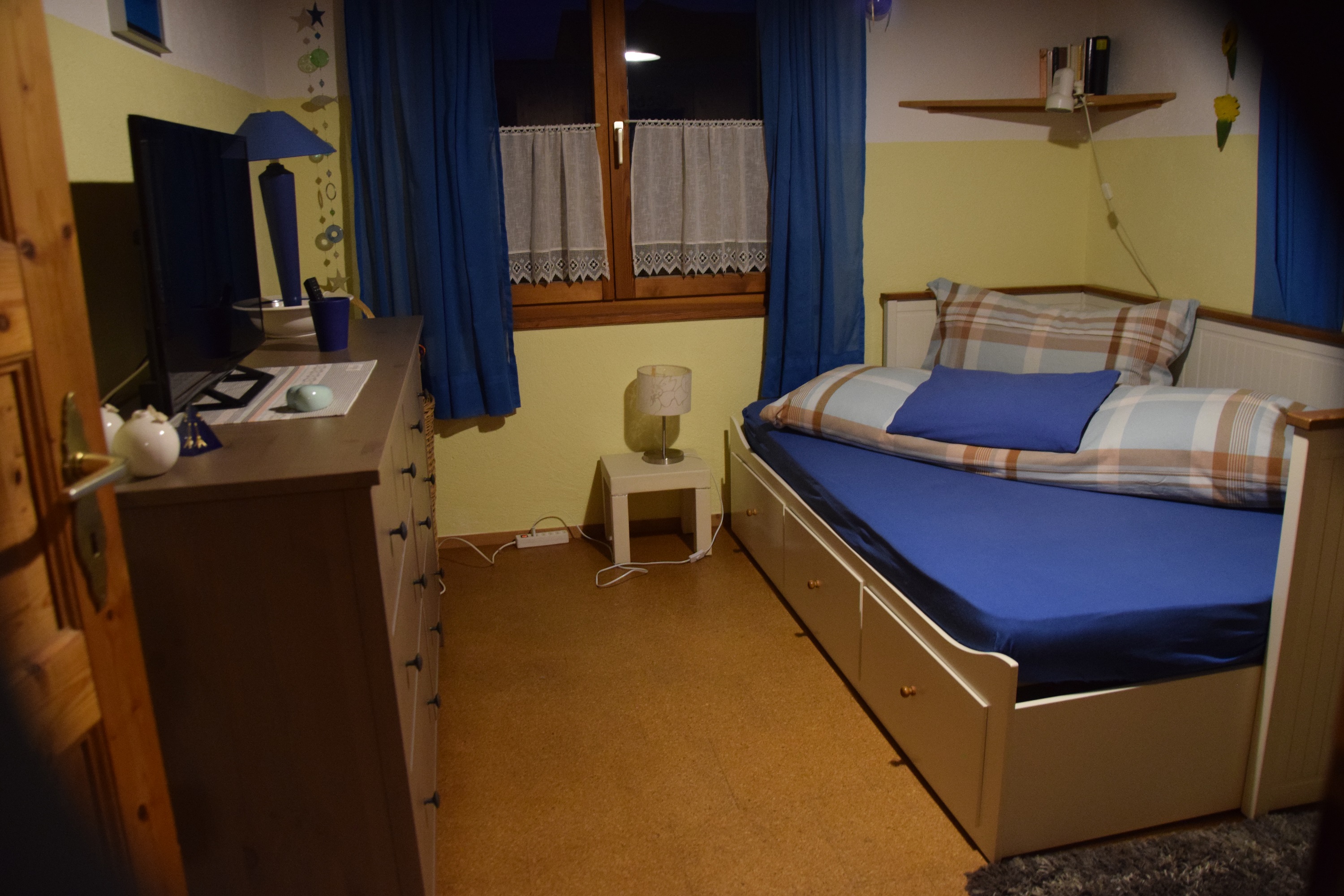 chlafzimmer im Studio in Eschen mit Bett, TV, Kommode und Fenster mit Vorhängen.